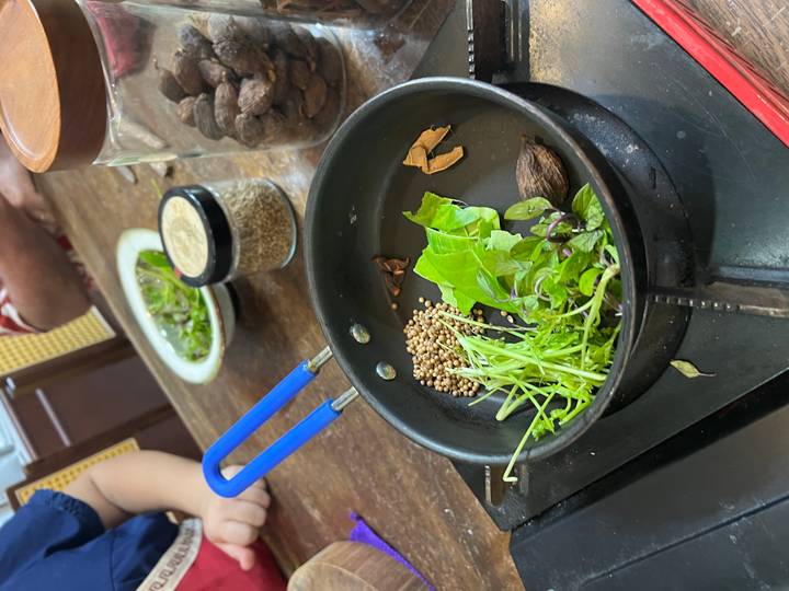 Saucepan with fresh herbs, seeds and spices being toasted for a cooking demonstration.