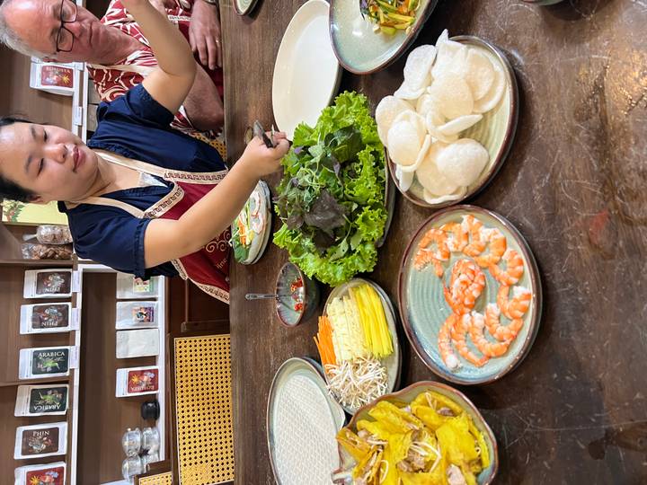 Instructor guiding participants around a table filled with prawns, herbs and rice crackers in cooking class.