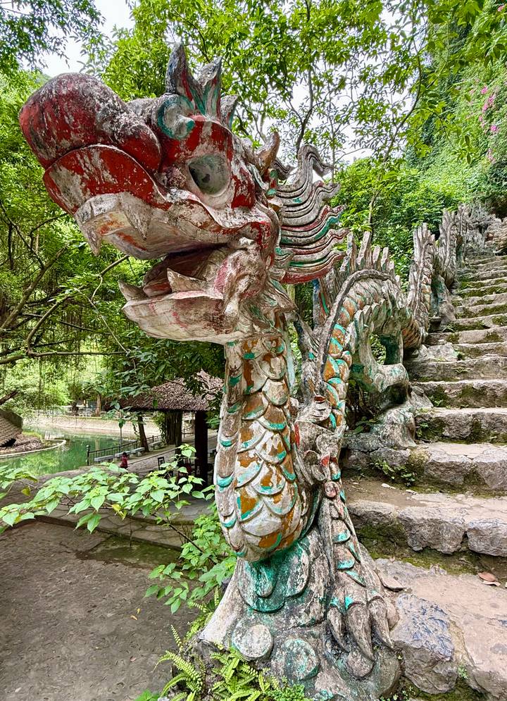 Colorful dragon sculpture lines a stone stairway in a lush forested temple setting.