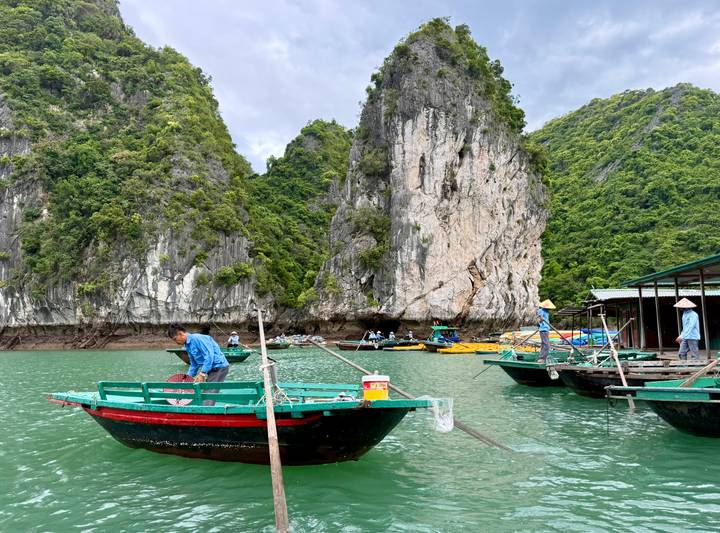 Small traditional boats float in emerald waters beneath towering limestone karsts.
