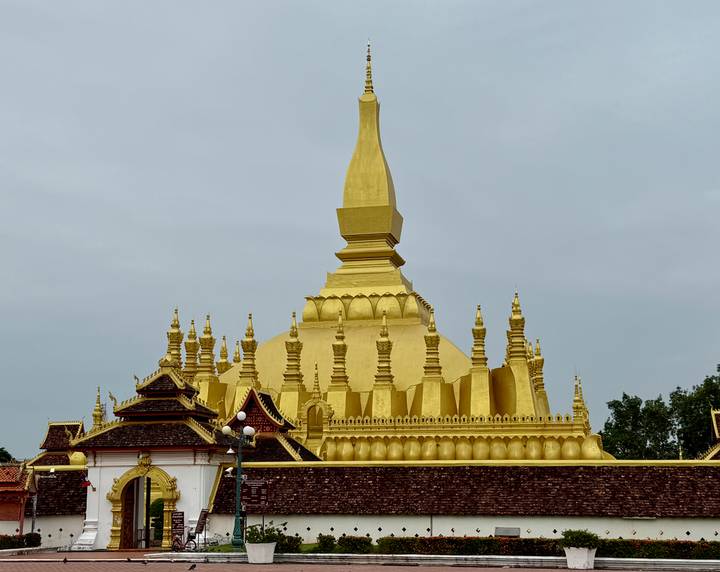 Golden stupa complex rises against a grey sky with ornate roofs and spires.