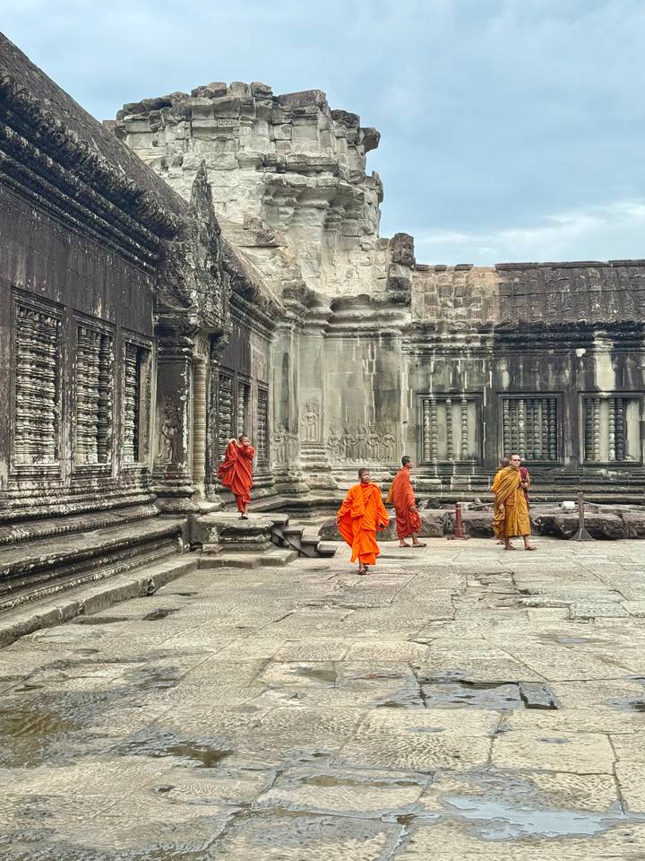 Buddhist monks in orange robes walk along the ancient stone galleries of Angkor Wat.