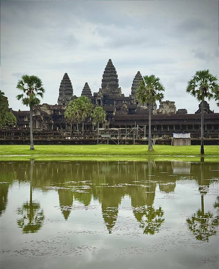 Angkor Wat main towers reflected in a moat with scaffolding on the ancient facade.