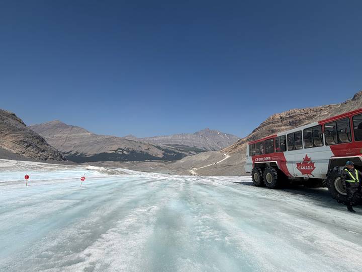 Ice Explorer bus parked on Columbia Icefield glacier with Rocky Mountains backdrop.