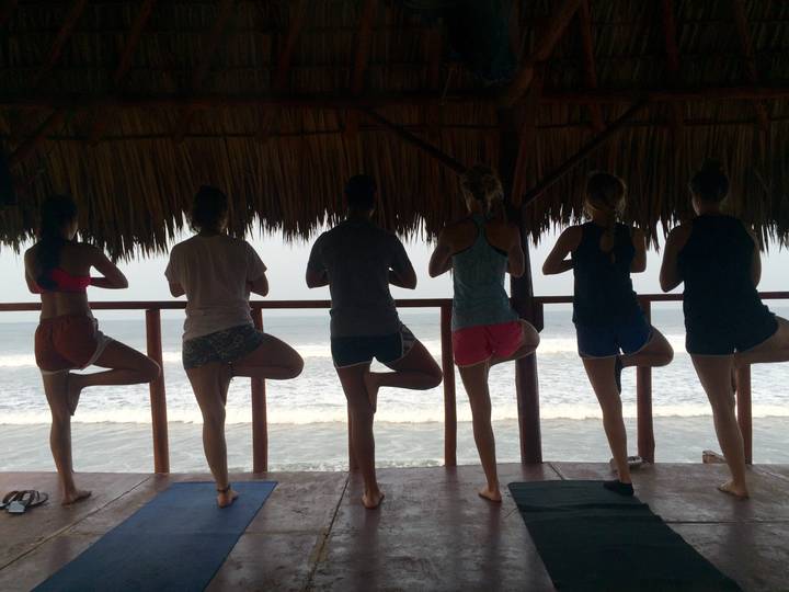 Group of people practicing yoga under a shelter overlooking the ocean.