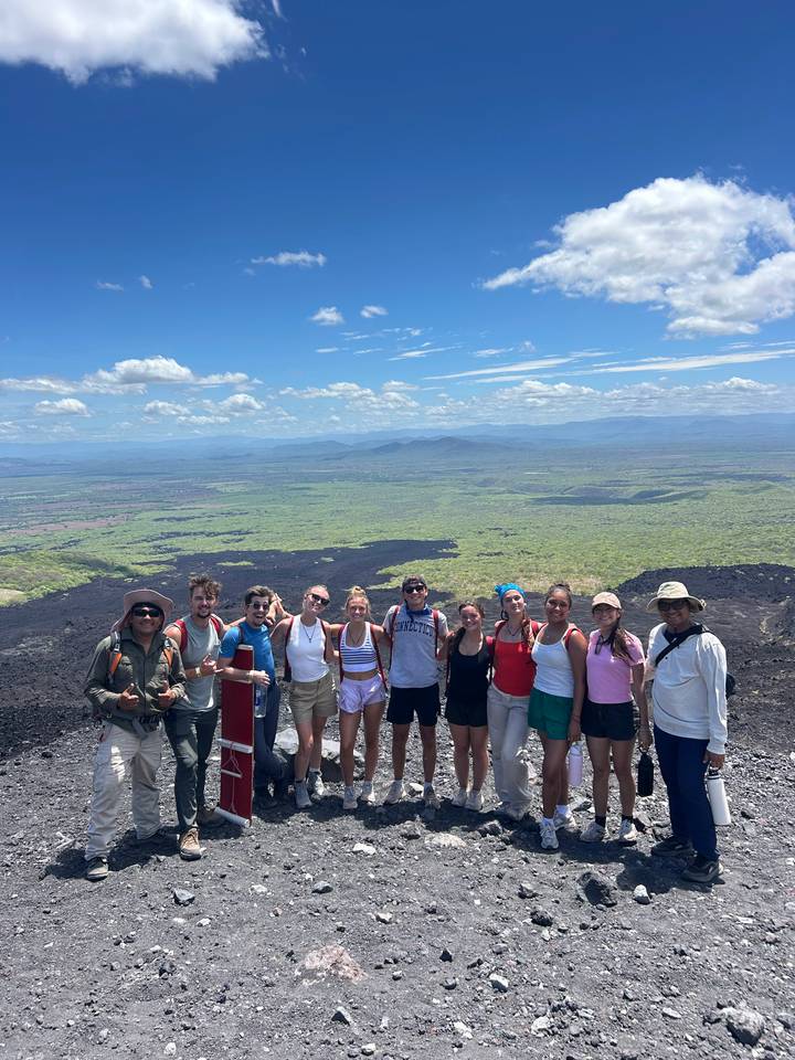 Hikers pose atop a volcanic ridge with vast green plains and black lava fields stretching below.