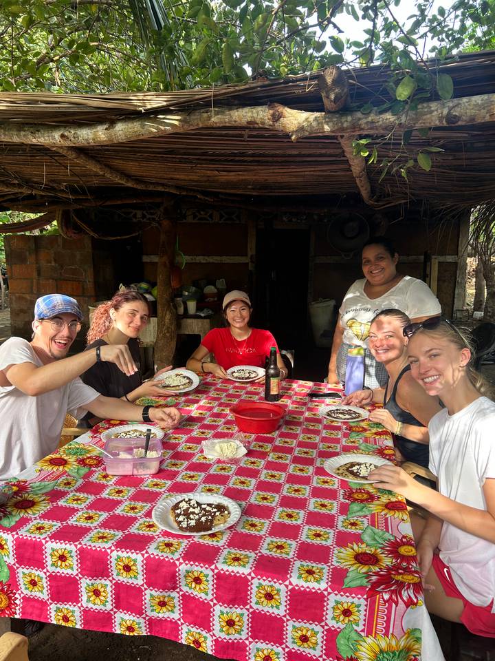 Travellers share a home-cooked meal at a colourful outdoor table with a local host.