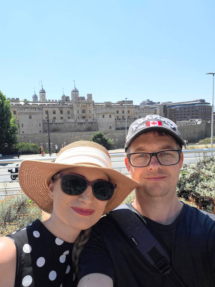 Selfie of a couple in front of the historic Tower of London on a sunny day.