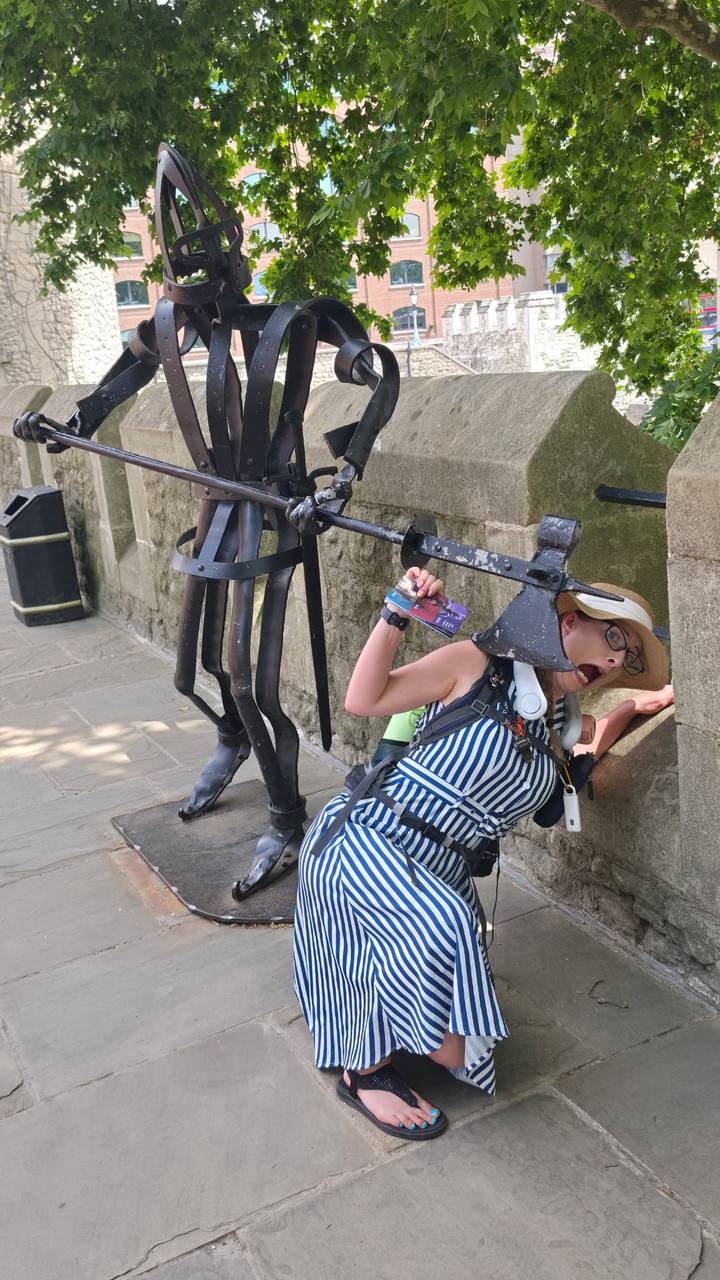 Tourist making a humorous face while posing under a medieval halberd display against stone walls