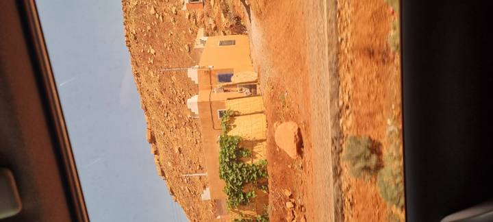 View from a car of a small desert house against a rocky hillside.