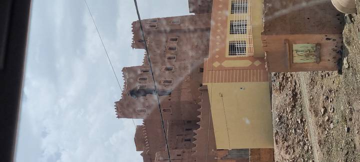 Brown kasbah-style fortress building photographed through a car window with reflections.