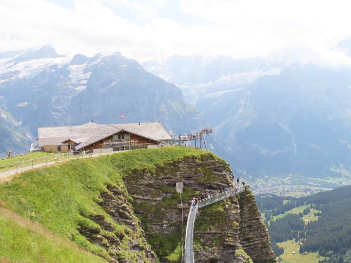 Clifftop restaurant and metal walkway overlook dramatic alpine valley and glaciers in Grindelwald.