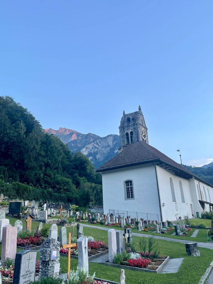 Historic stone church tower set against forested mountains glowing in soft evening light.