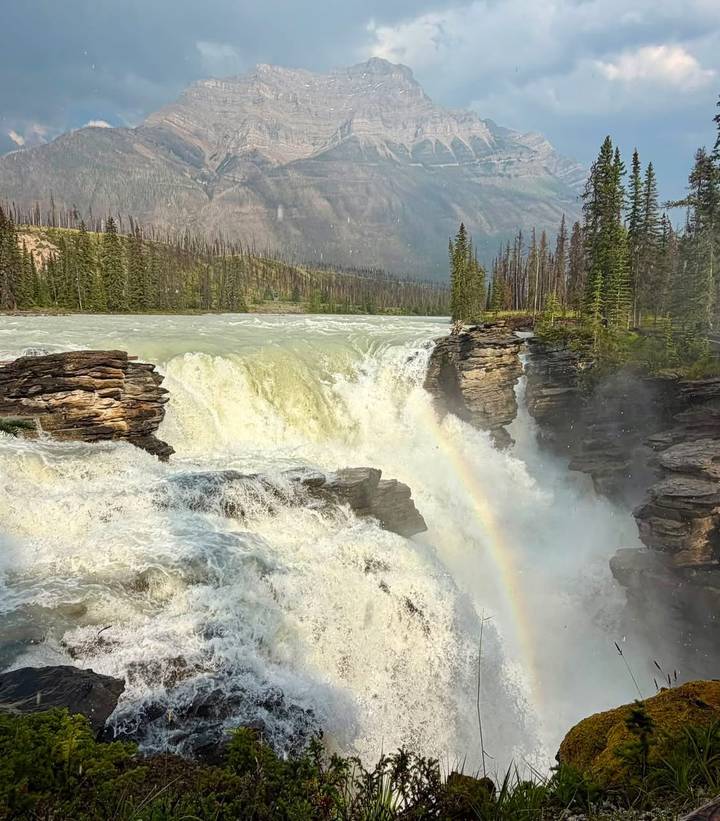 Powerful waterfall crashing through a rocky canyon with a visible rainbow in the mist.