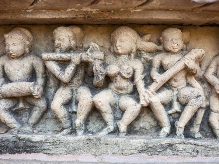 Weathered stone relief of musicians and dancers carved into the base of an ancient Indian temple.