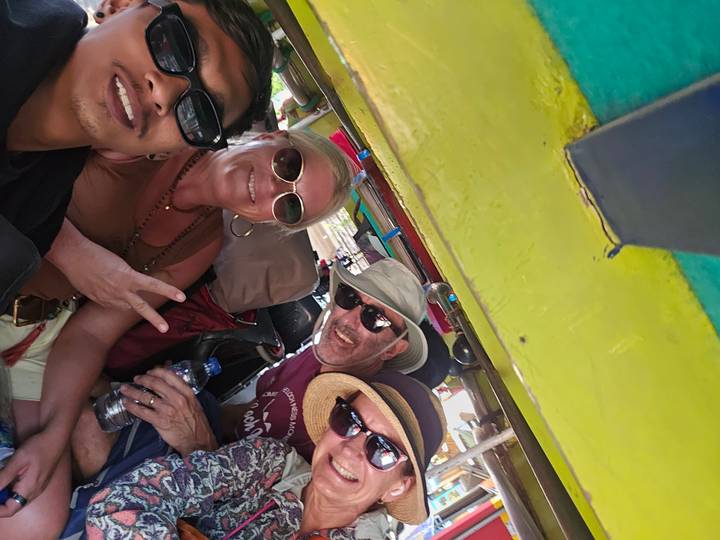 Repeat selfie of four travellers smiling inside a colourful three-wheeled vehicle.