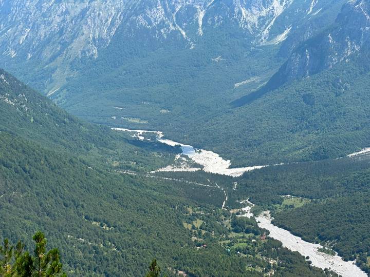 Expansive alpine valley with winding white river surrounded by dense green mountains.