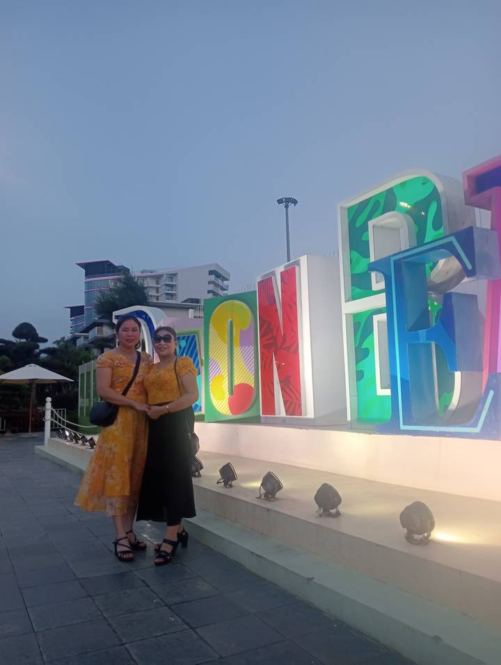 Two women posing in front of large colorful letter sculpture in modern outdoor plaza at dusk.