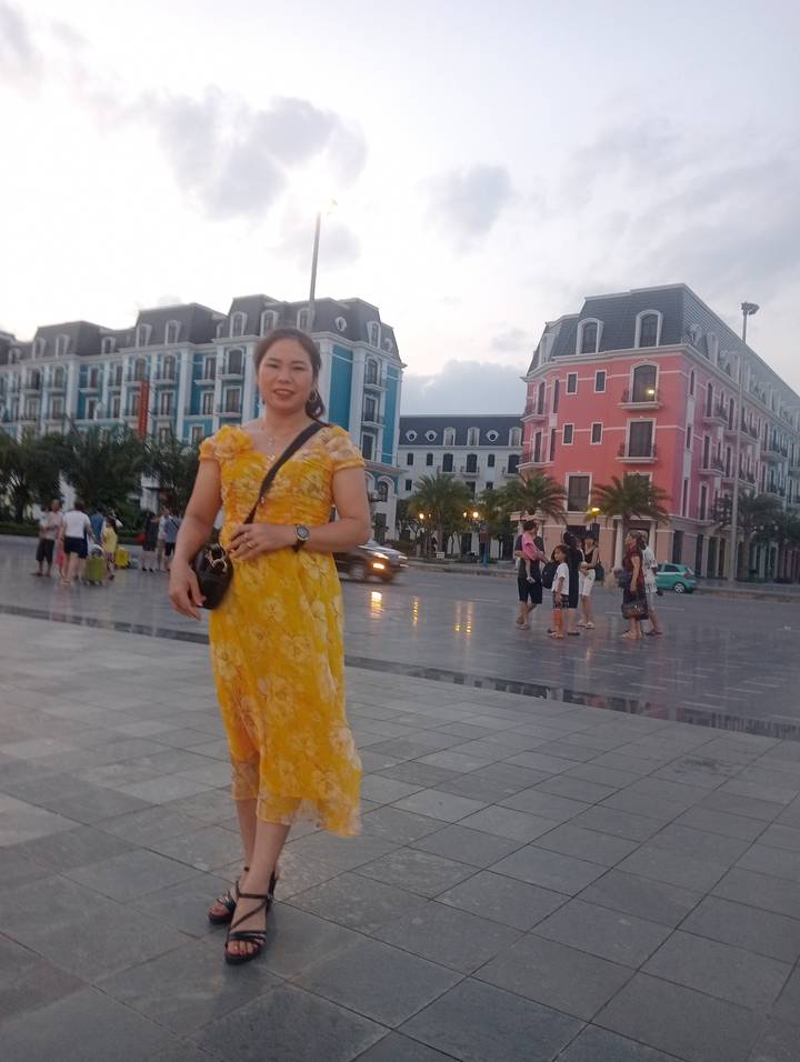 Woman in yellow dress smiling in front of colourful European-style buildings and plaza.