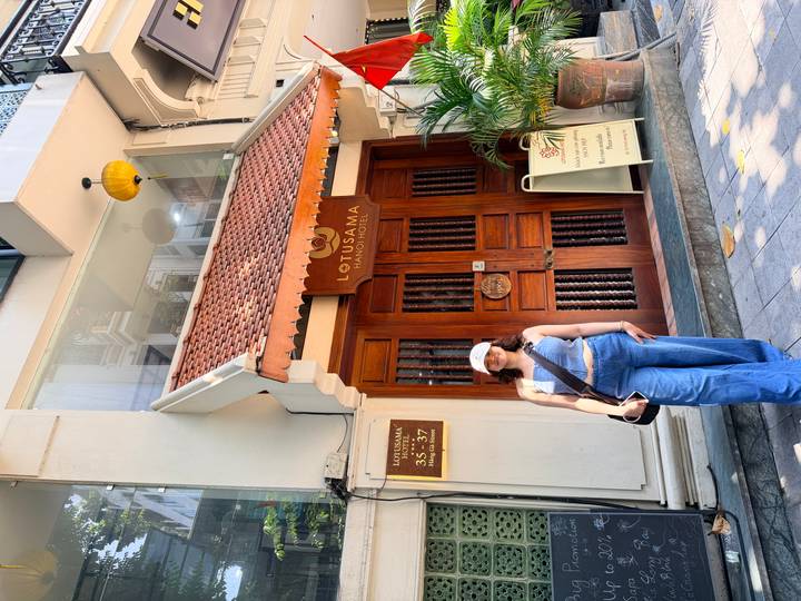 Visitor smiles outside the Lotusama Hanoi Hotel entrance holding a tote bag.