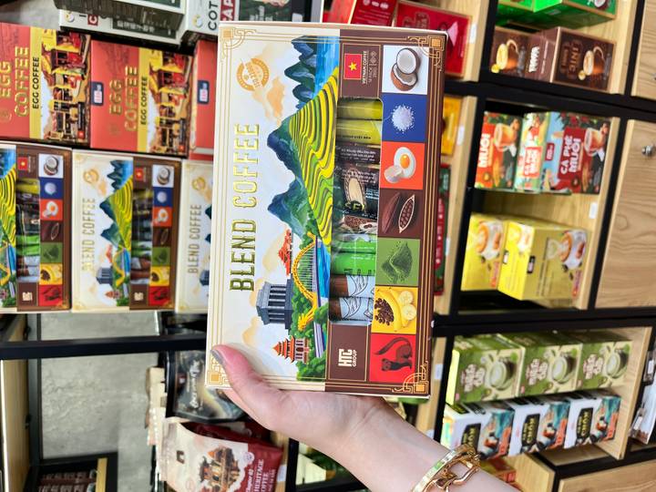 Hand holds a colorful Vietnamese coffee gift box labeled Blend Coffee in a souvenir shop.