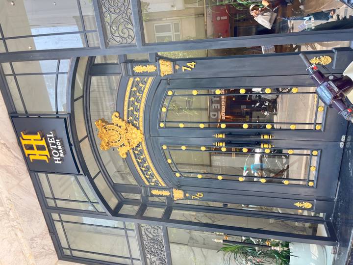 Grand black and gold arched doorway of Hotel Hanoi with reflections of city life in the glass.