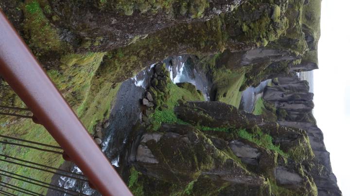 Vertical vista of moss-covered Fjadrargljufur canyon with river flowing far below.