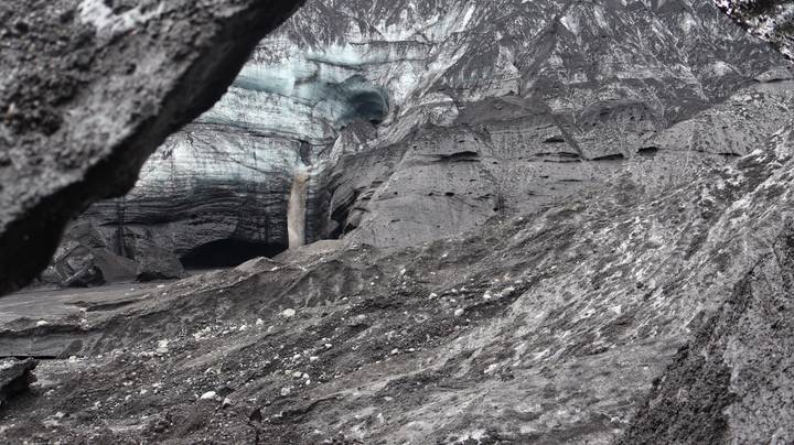 Dark volcanic ash gorge revealing vivid blue ice cave and waterfall of Skaftafell glacier.