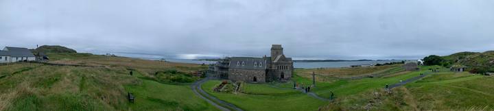 Panoramic view of grey-stone Iona Abbey under renovation, overlooking the rugged coastline and rolling lawns.