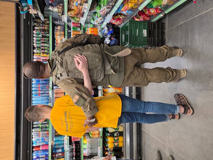 Casual moment of a soldier and a friend with arms around each other while browsing a brightly stocked drink fridge.