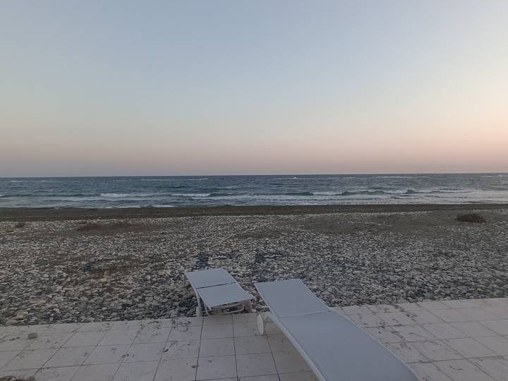 Quiet pebble beach with two empty loungers facing gentle evening waves and pastel sky