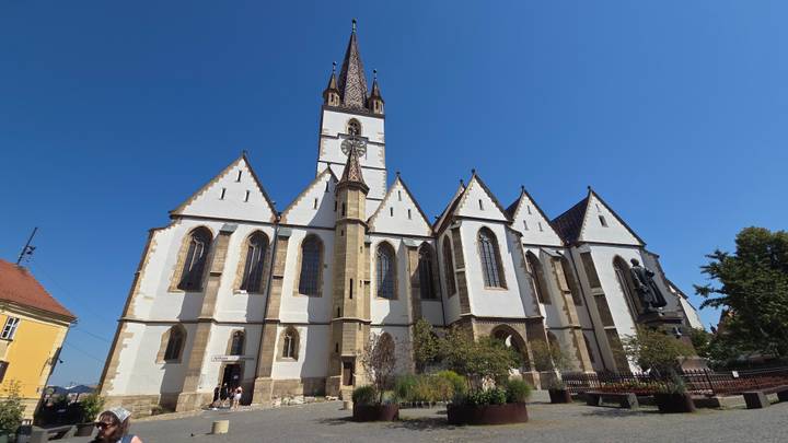 Wide view of the white-walled Lutheran Cathedral with tall spire rising against a cloudless blue sky in a cobbled square.