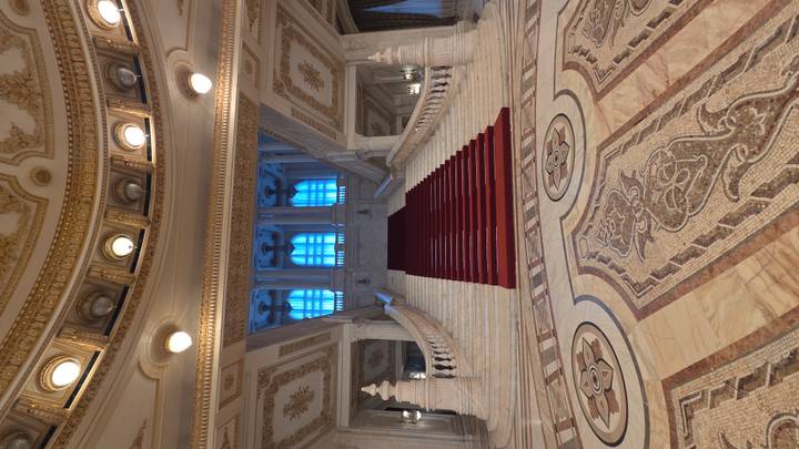 Grand marble staircase with red carpet and ornate ceilings inside the Palace of Parliament.