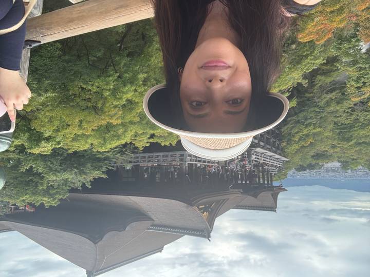Traveller takes a selfie with Kyoto's wooden Kiyomizu-dera temple perched above the forested hillside.