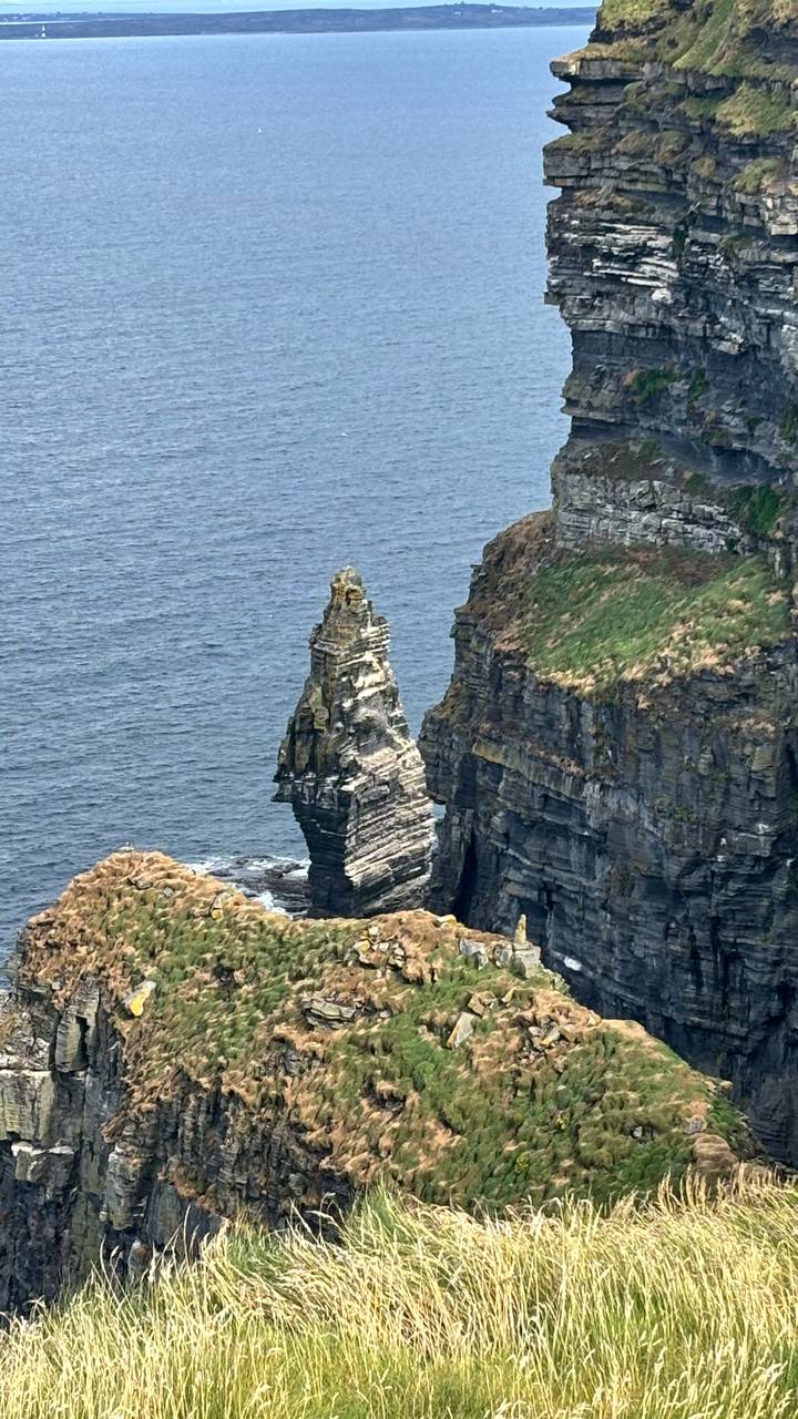 Jagged sea stack rising from the Atlantic below sheer green cliffs.