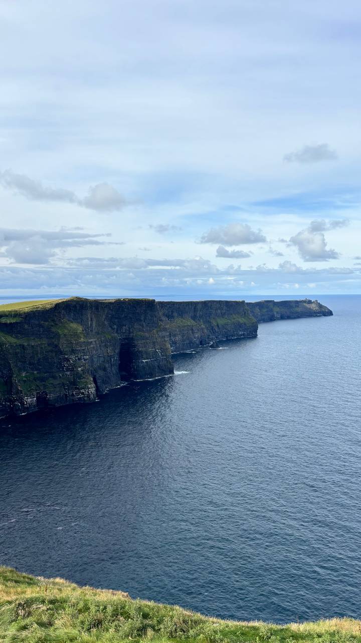 Sweeping panorama of the Cliffs of Moher stretching into the Atlantic under dramatic cloud cover.