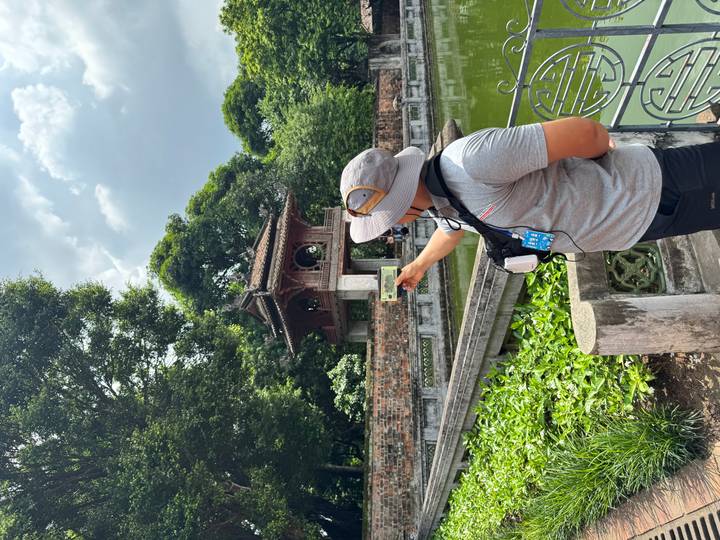 Guide holds banknote to match the historic pavilion behind at Temple of Literature.
