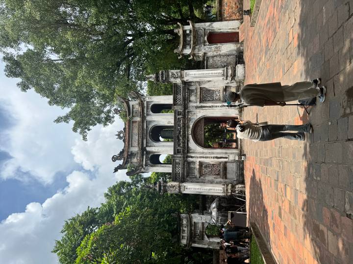 Visitors photograph each other in front of an ornate stone gateway inside a historic complex.