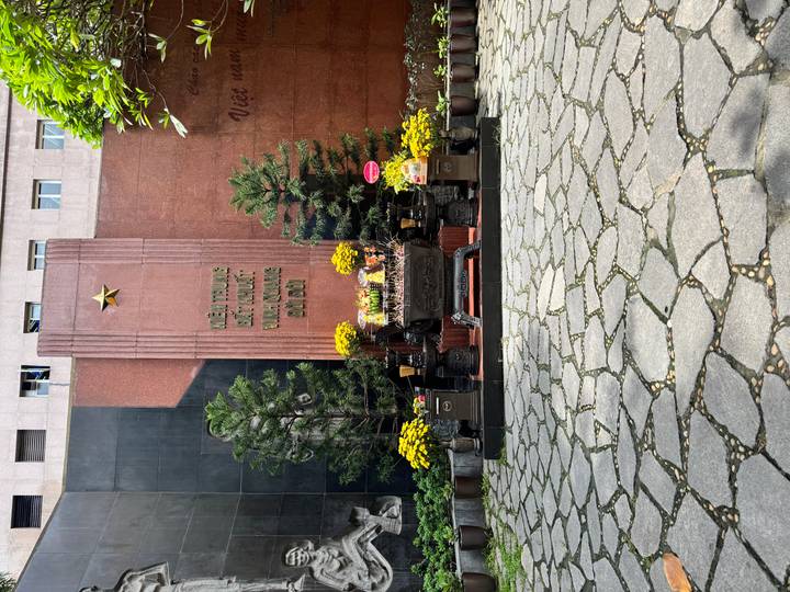 Outdoor memorial altar with yellow flowers and Vietnamese inscription set against stone walls.