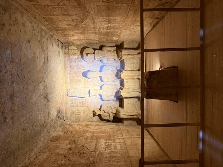 Interior chamber with four illuminated seated statues carved into sandstone walls.