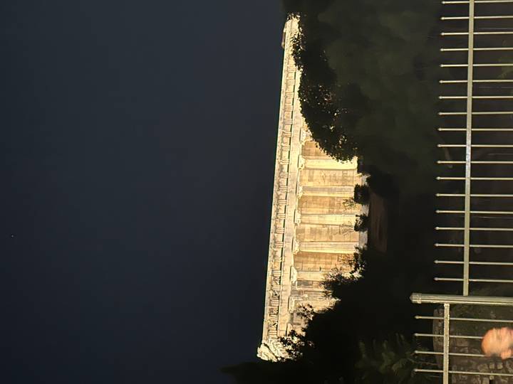 Nighttime view of an illuminated classical Greek temple partially hidden behind trees.