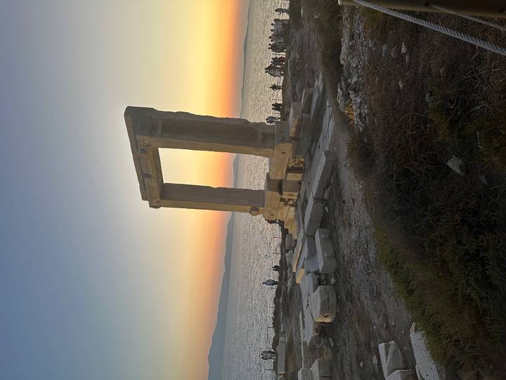 The Portara gateway of Naxos silhouetted against a colorful Aegean sunset.