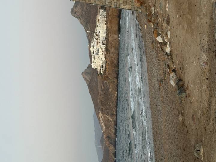 Rocky shoreline with small white village clinging to a cliff above choppy sea.
