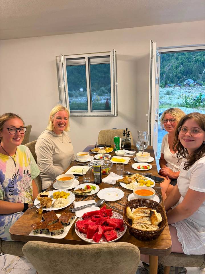 Four travellers seated around a dinner table enjoying soup and Albanian cuisine indoors.
