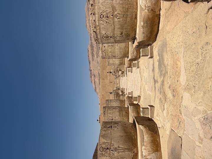 Stone courtyard lined with massive carved jars and statues amid ancient temple ruins.