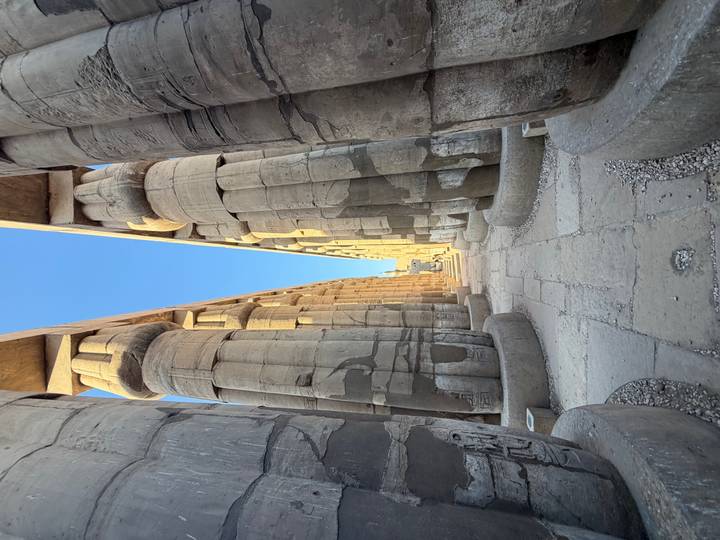 Long perspective between colossal sandstone columns of an ancient Egyptian temple lit by morning sun.