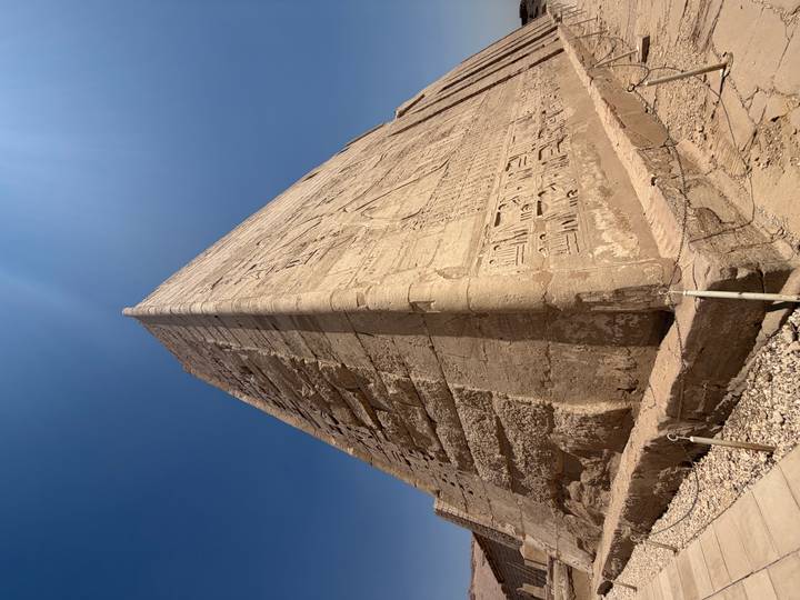 Massive sandstone wall corner covered in hieroglyphs basking in bright desert sun.