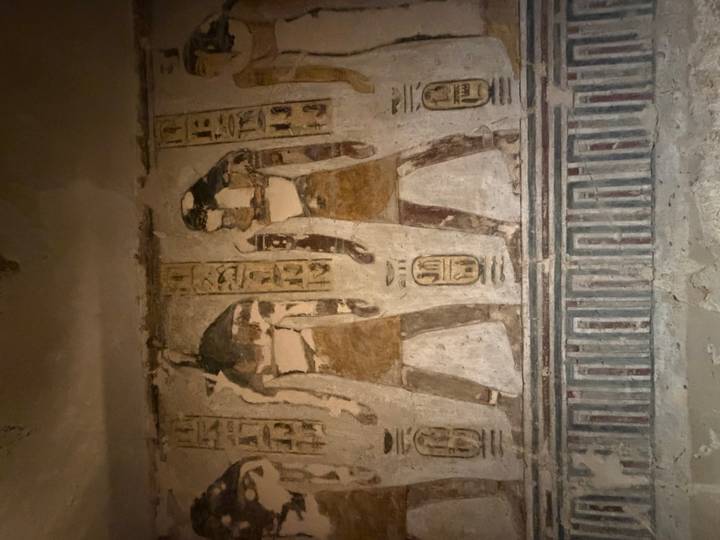 Faded wall painting depicting ancient figures with hieroglyphic inscriptions inside a tomb.