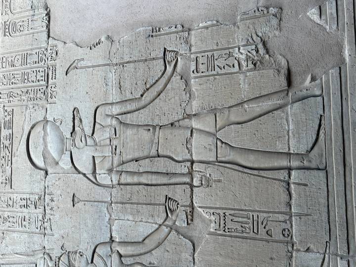 Relief carving of an Egyptian deity etched into a large stone temple wall.