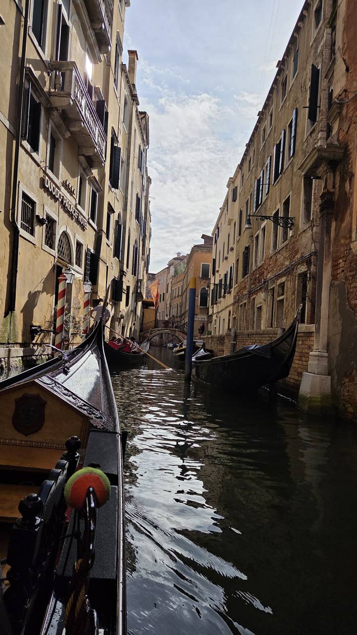 Narrow Venetian canal lined with gondolas and pastel buildings under soft light.